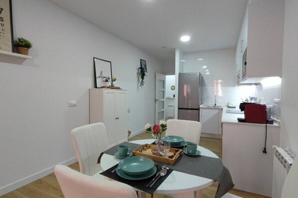 A modern kitchen with white cabinetry, a stainless steel refrigerator, and a dining area with a round table and chairs.