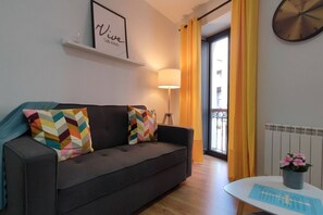 A modern living room with a sofa, colorful cushions, a lamp, a small table with a plant, and a framed quote on the wall.