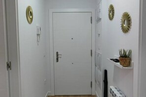 A hallway with a white door, decorative wall sconces, and a small shelf with a plant.