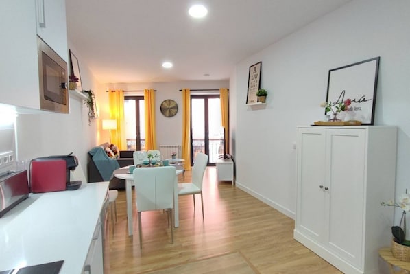 Un appartement moderne comprenant une cuisine, un coin repas et un salon. On y trouve un meuble blanc, une table à manger avec des chaises et un canapé.