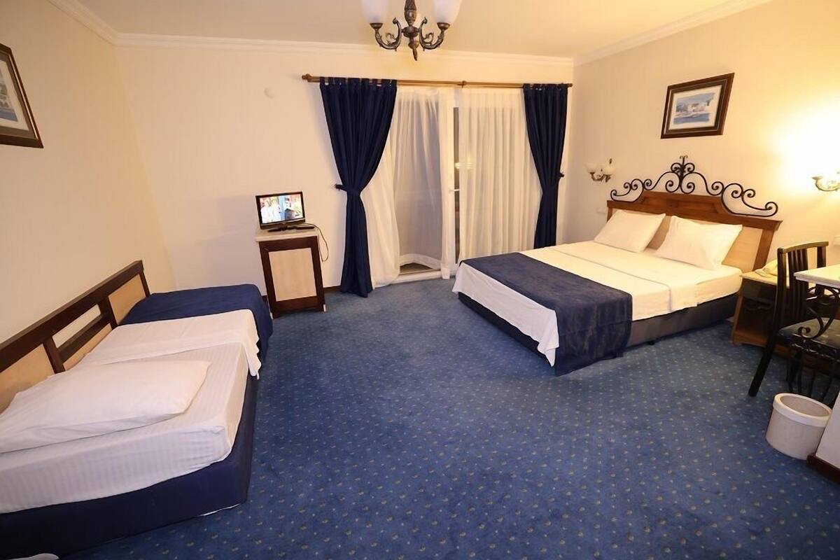 Ein Hotelzimmer mit zwei Betten, einem kleinen Tisch mit Fernseher, einem Sessel und einem Fenster mit Vorhängen.