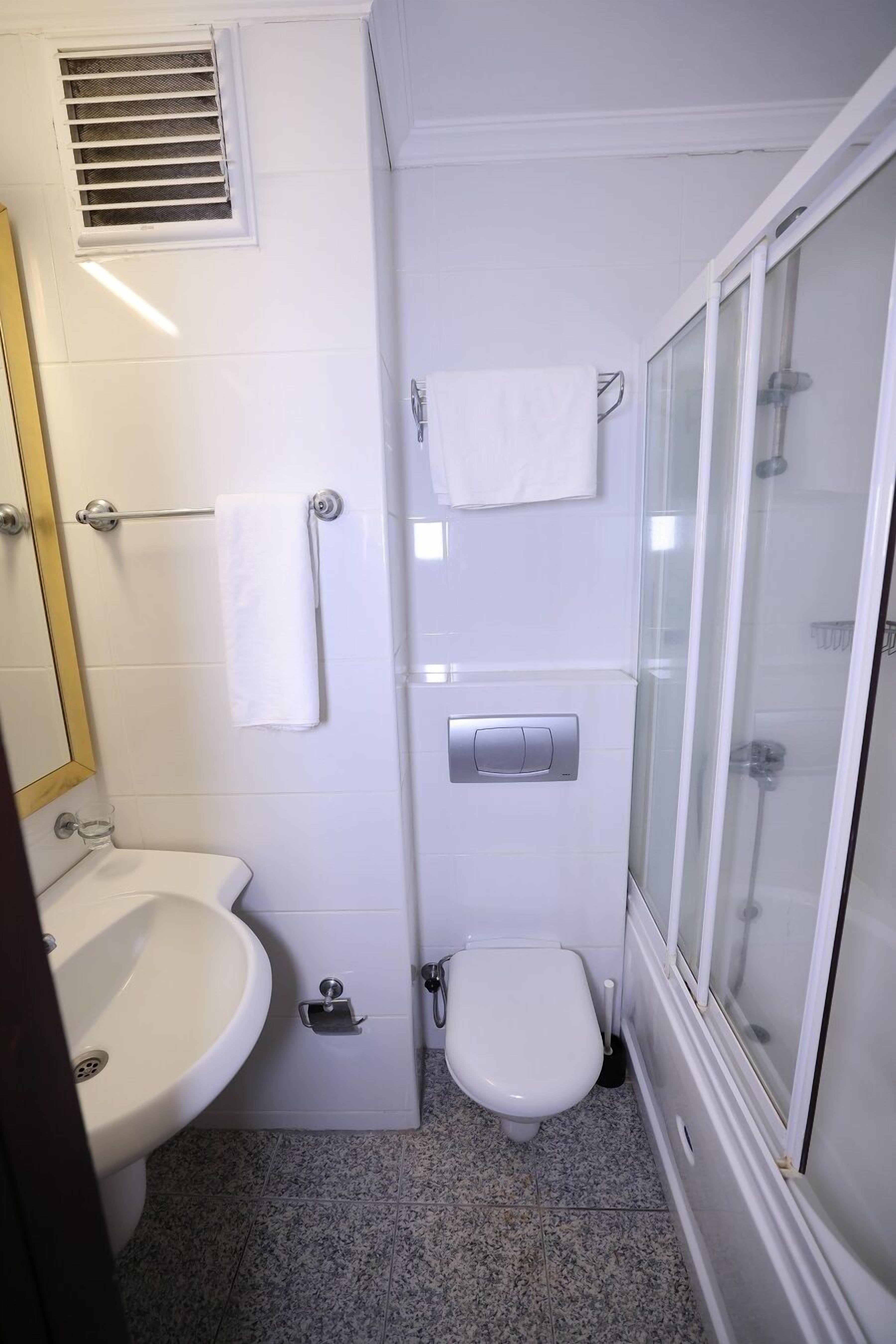 Casa de banho compacta com lavatório branco, sanita e cabine de duche com parede de vidro.
