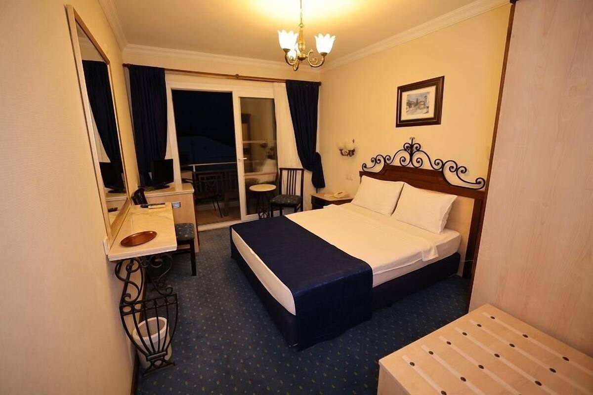 Ein Hotelzimmer mit Bett, Schreibtisch, Stuhl, kleinem Tisch und einem Balkon mit Sitzgelegenheit.