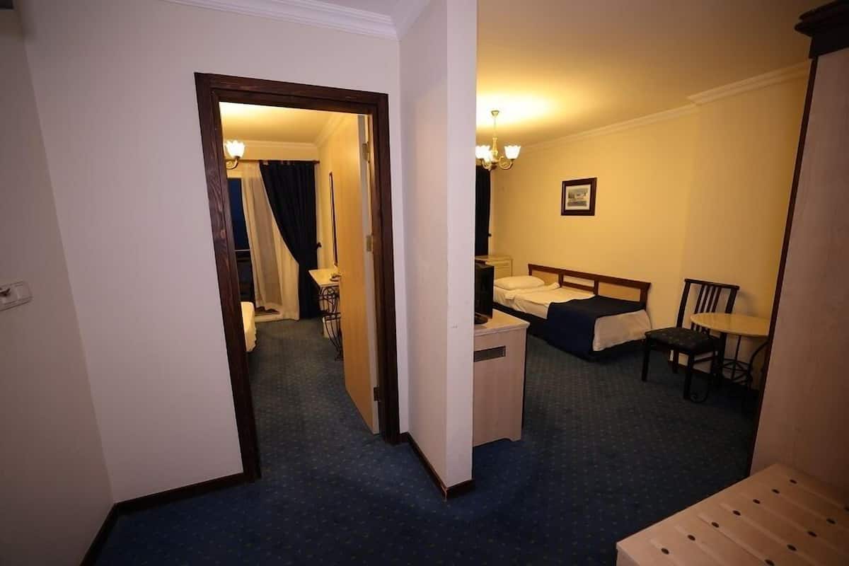 Ein Hotelzimmer mit einem Bett, einem Schreibtisch, einem Stuhl und einem kleinen Tisch. Eine Tür führt in einen anderen Raum.