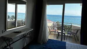 Une chambre d’hôtel avec un balcon donnant sur la mer, un lit, un bureau et une chaise.