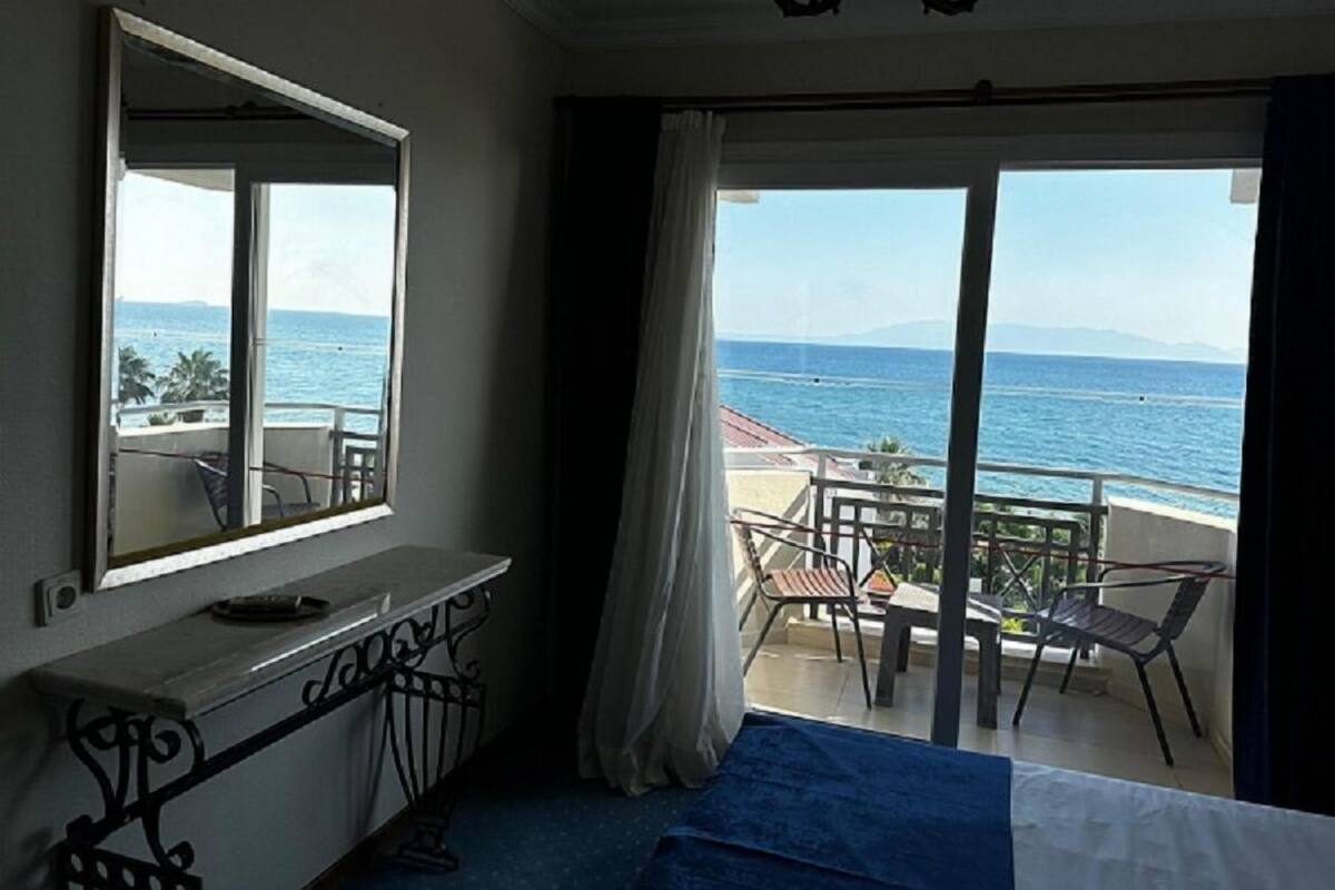 Ein Hotelzimmer mit Balkon und Meerblick, ein Bett, ein Schreibtisch und ein Sessel.