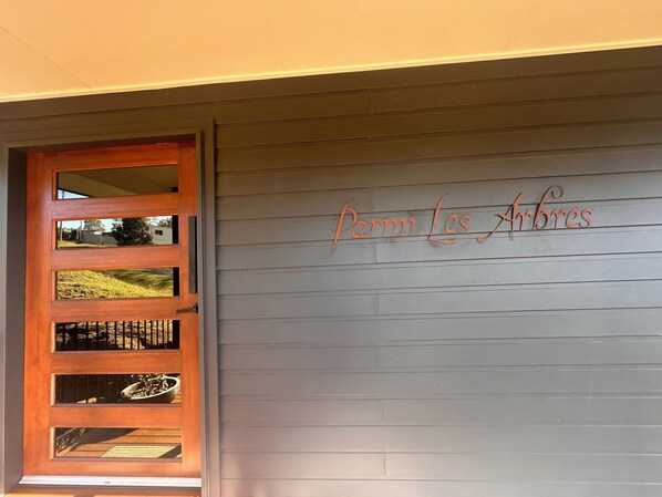 Una puerta de madera con un panel de vidrio y una pared gris con el texto 'Panni Les Arbres' escrito en ella.