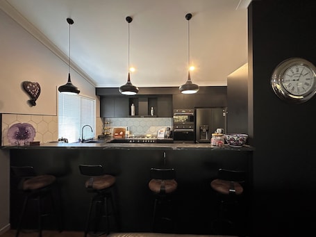 A modern kitchen with pendant lighting, a central island with bar stools, a refrigerator, and a clock on the wall.. Self Check In, getaway with stunning views of Boomerang Lagoon and Mt Kooralbyn.
