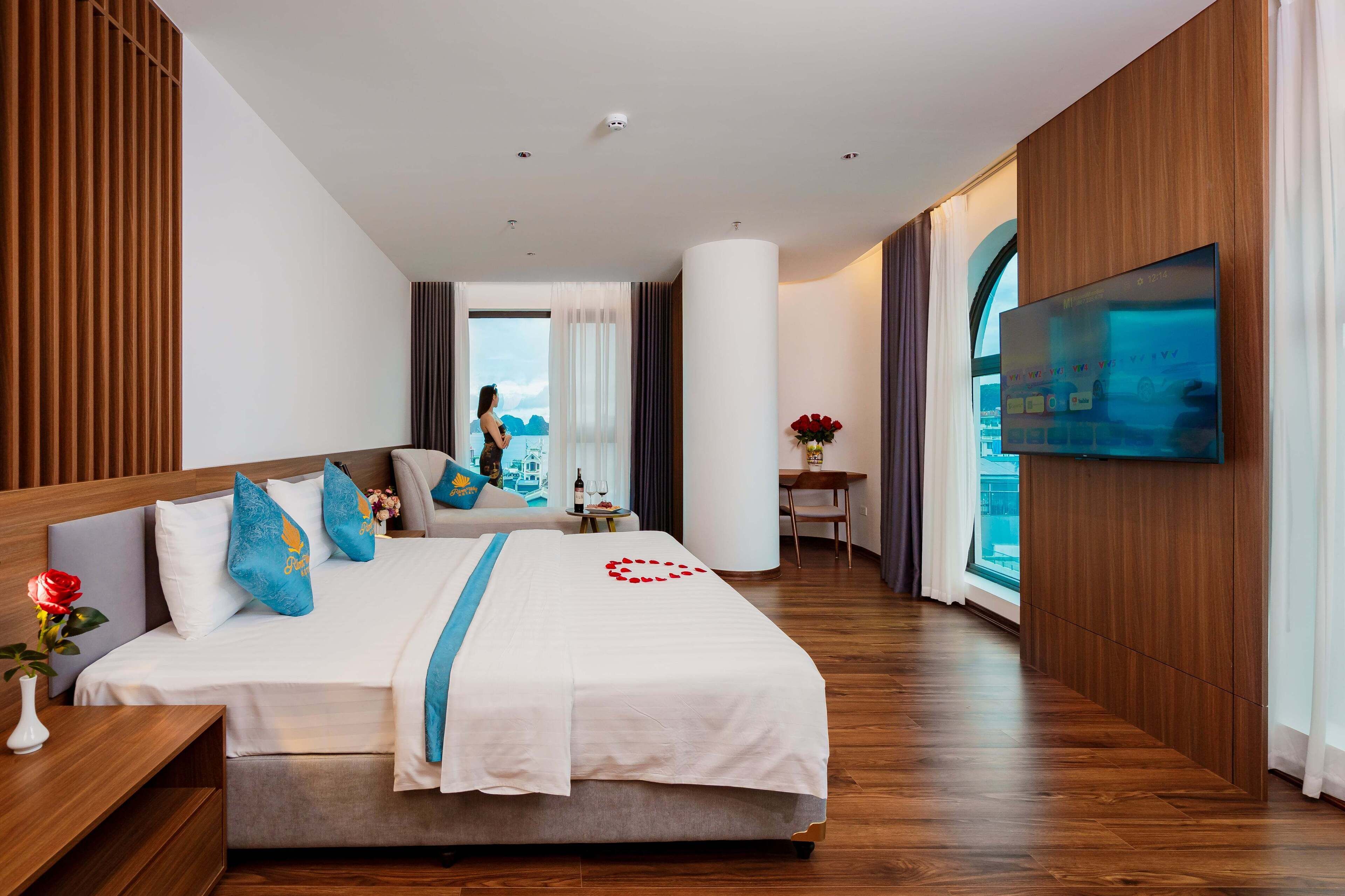 Una habitación de hotel moderna con una cama grande, paneles de madera, un televisor de pantalla plana y vistas a la ciudad.