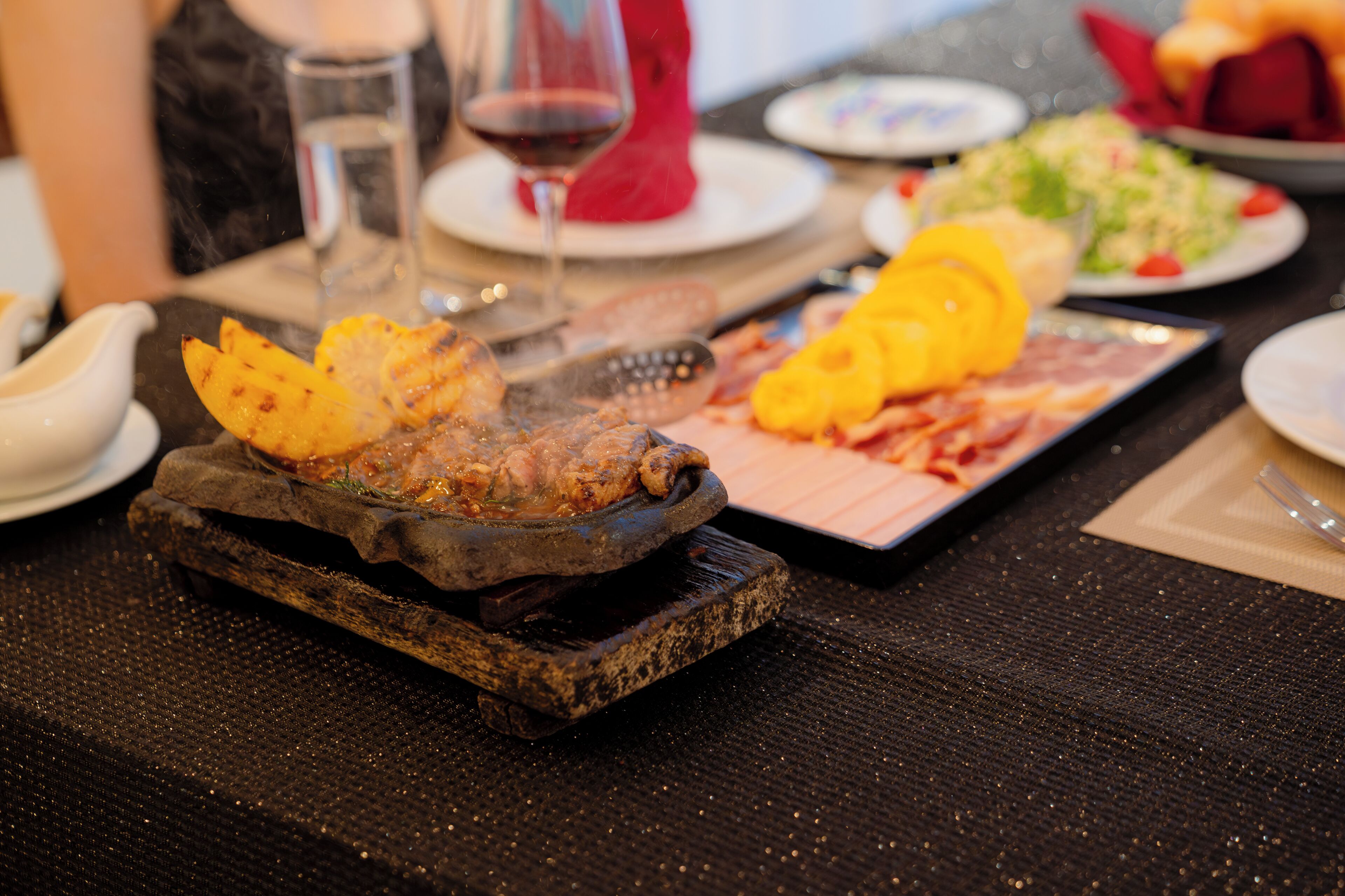 A dining table with a variety of dishes including grilled meat, vegetables, and a glass of red wine.