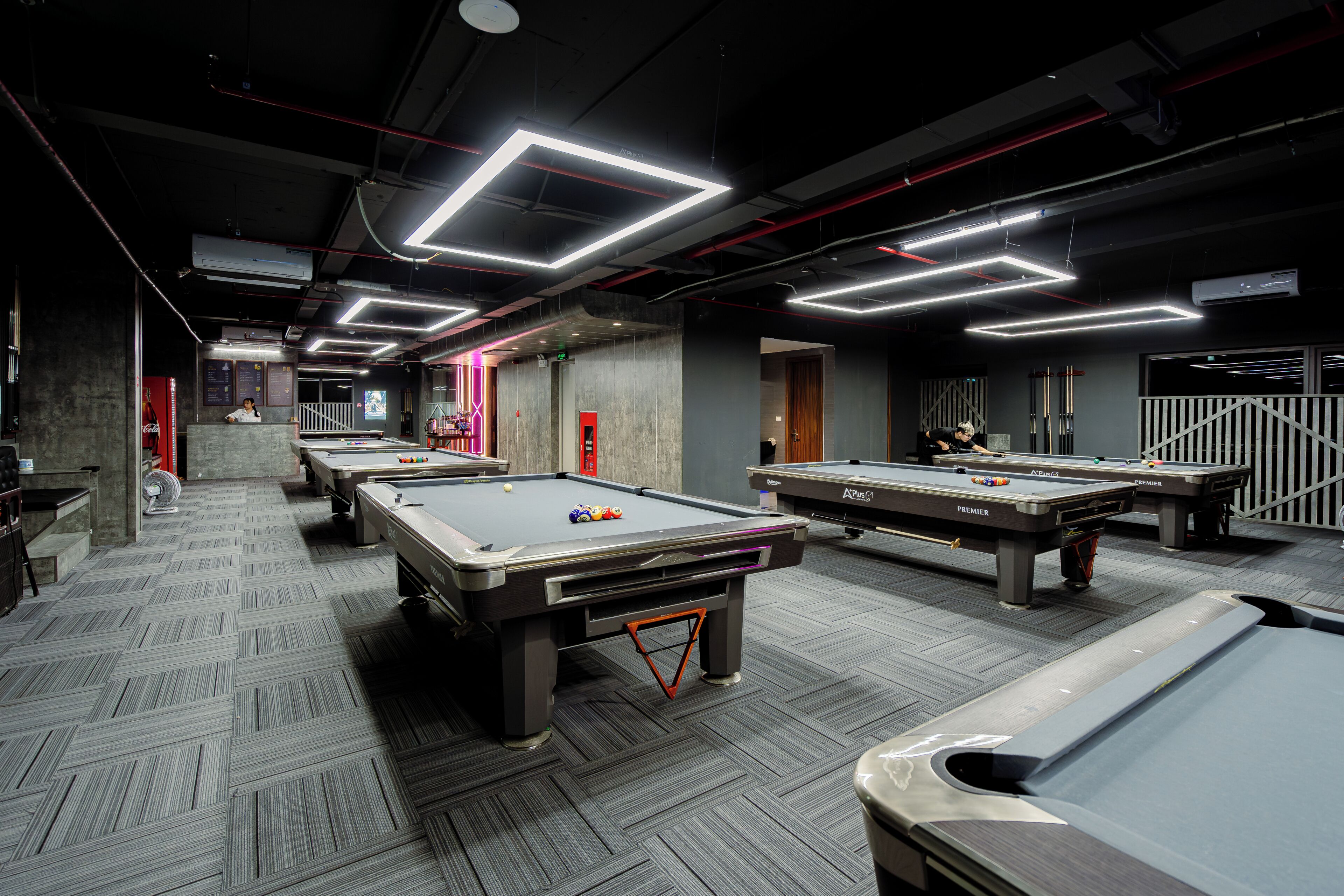 A pool hall with multiple tables and a herringbone-patterned floor.
