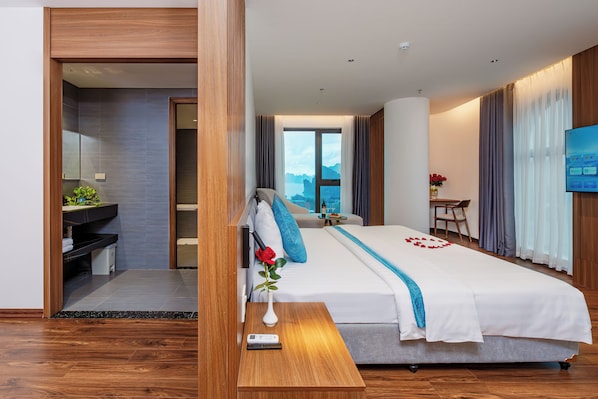 A modern hotel room with a large bed, a bedside table, a TV, and a view of the mountains.