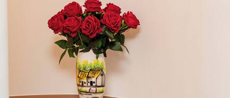 A wooden table with a white chair, a vase with red roses, and a book on the table.