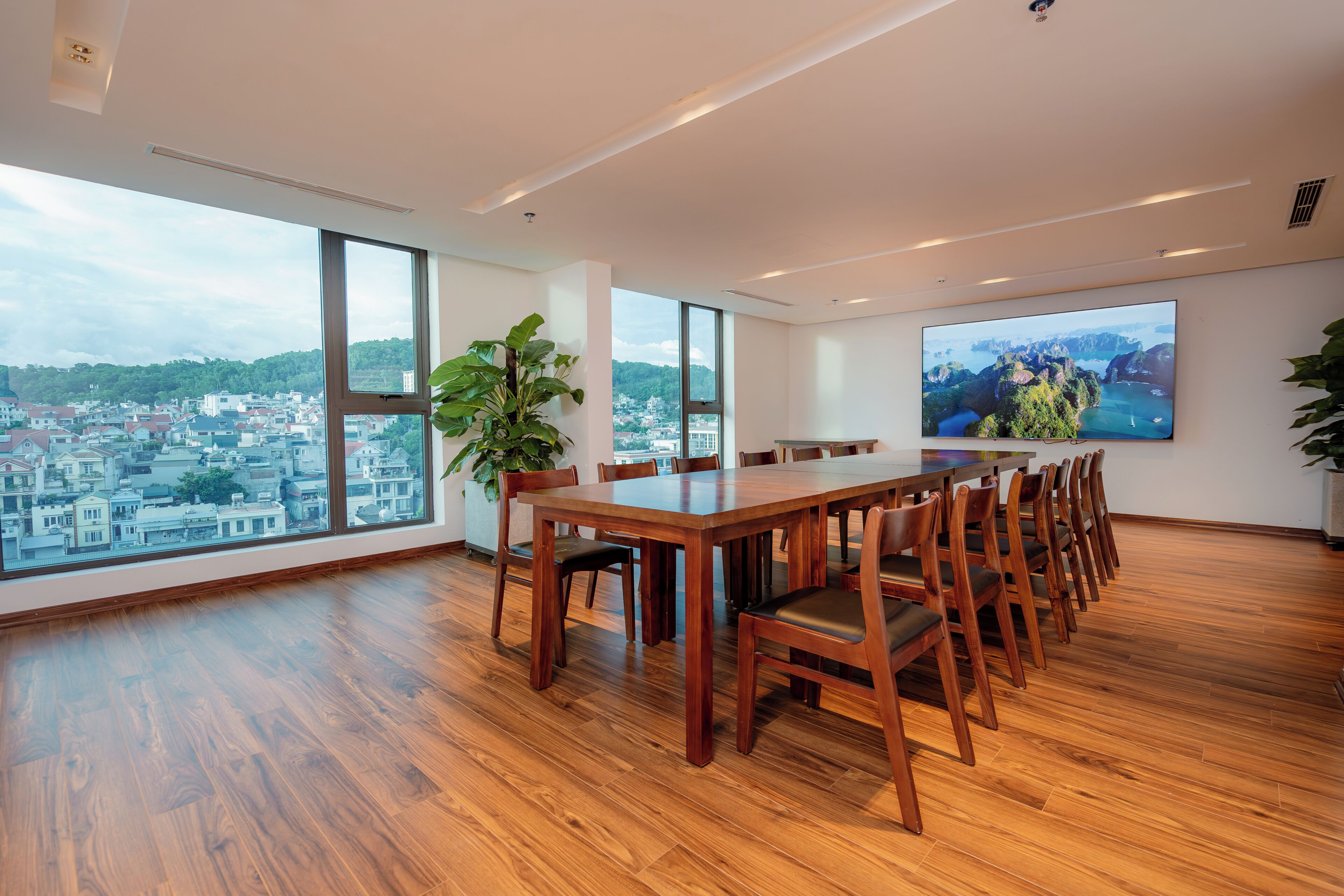 Una amplia sala de conferencias con una gran mesa y sillas, ventanas grandes con vistas a la ciudad y un televisor montado en la pared.