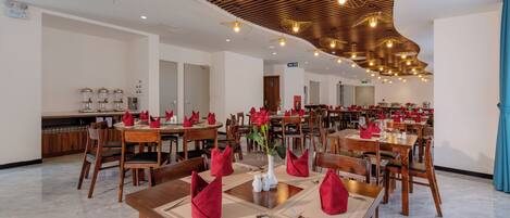A spacious dining area with wooden tables, red napkins, and modern pendant lighting.