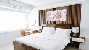 Un dormitorio moderno con estructura de cama de madera, ropa de cama blanca, una mesita de noche con lámpara y un tablero auxiliar con espejo, además de una obra de arte floral en la pared.