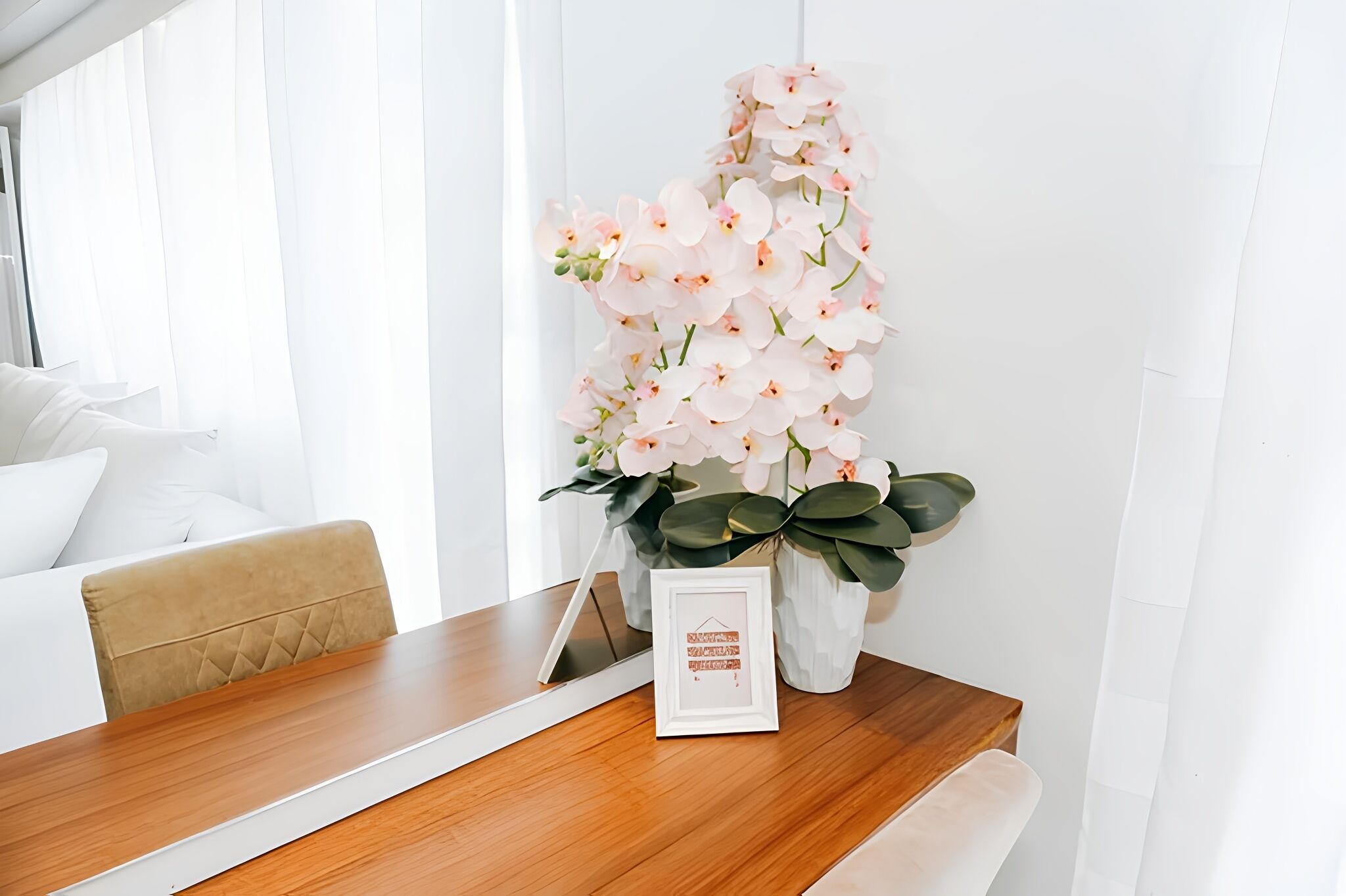 Una mesa de comedor con un cuadro enmarcado, un jarrón con flores rosas y una planta.