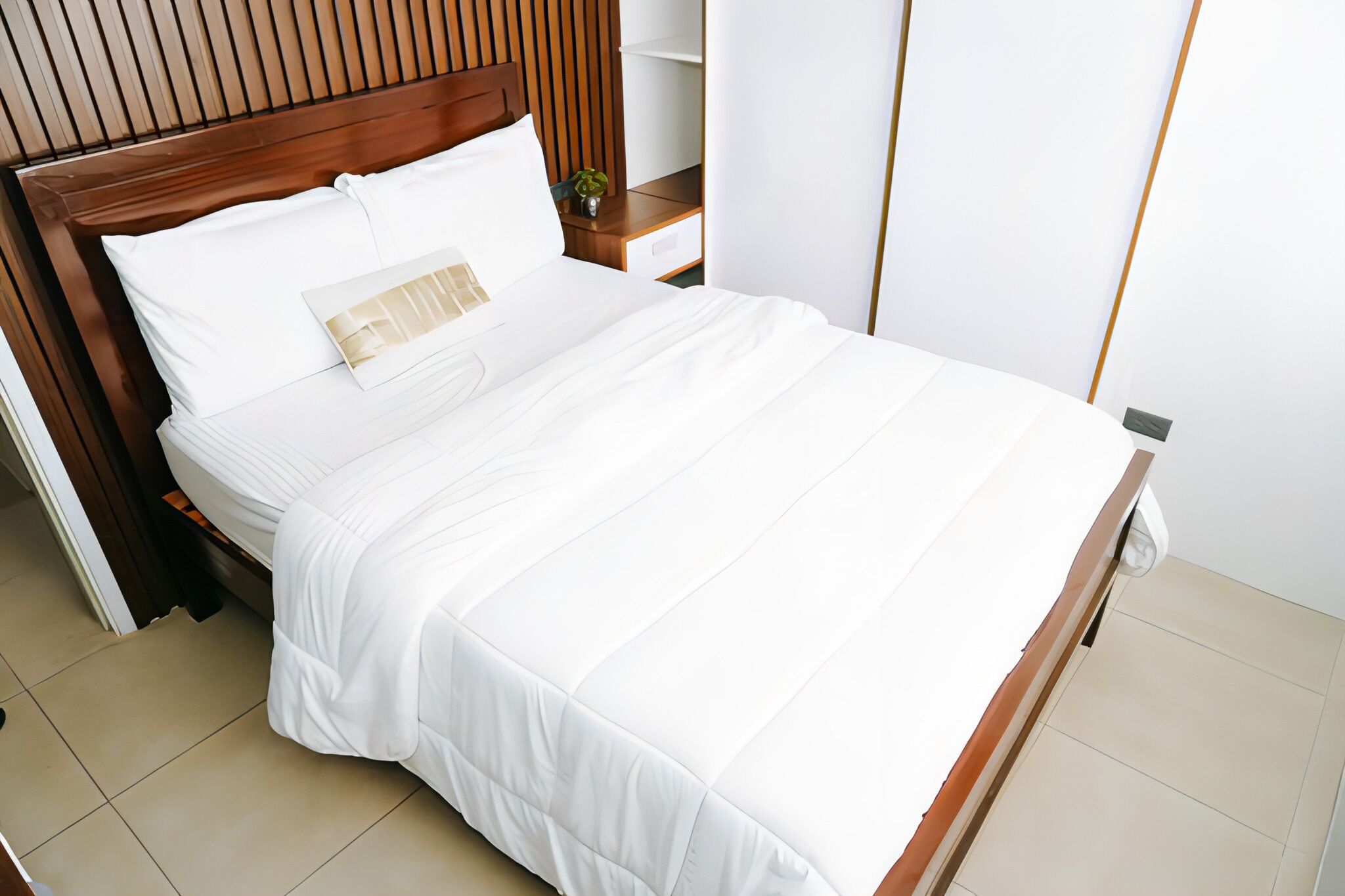 A neatly made bed with white linens and a wooden headboard.