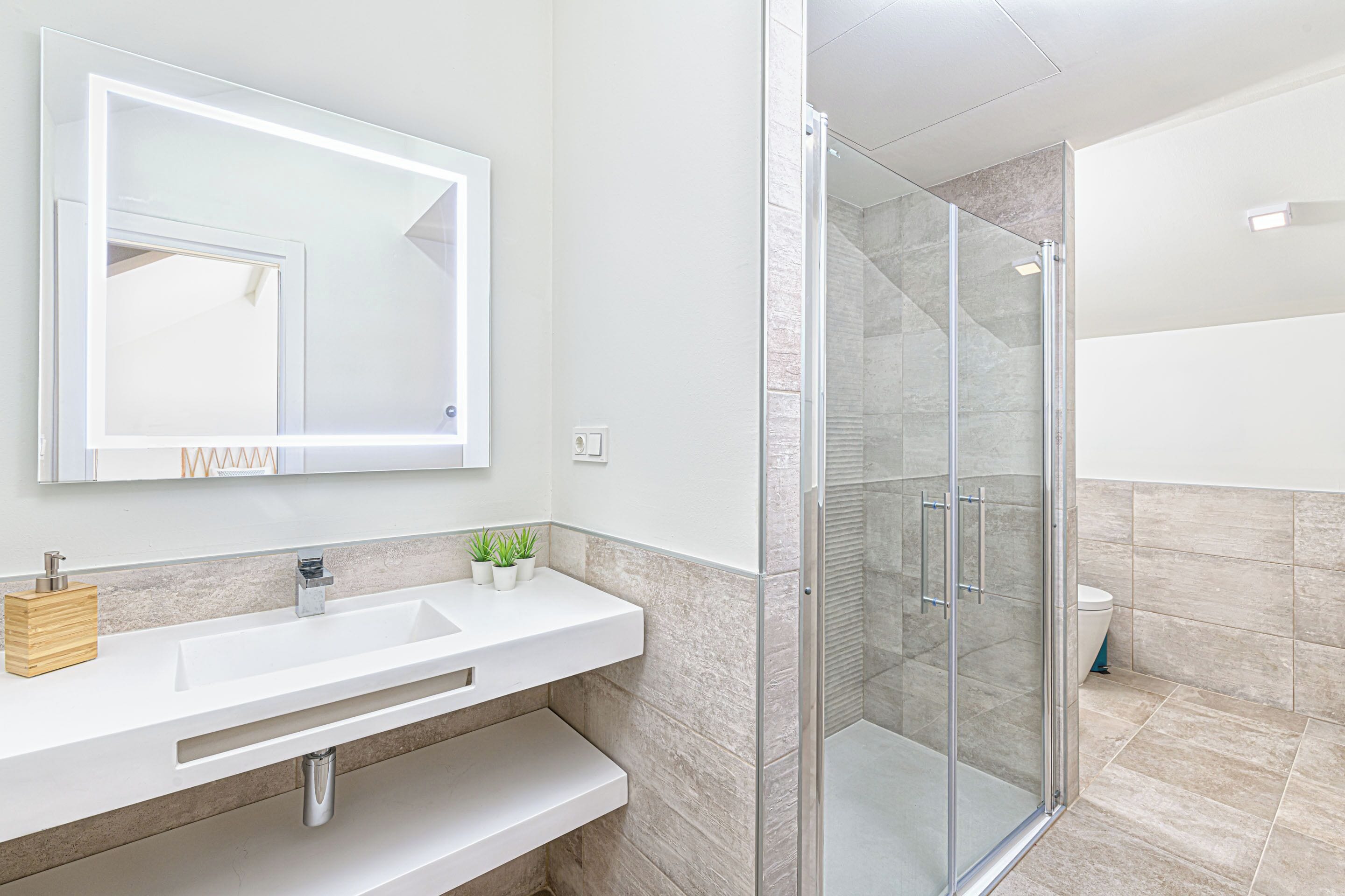 Een moderne badkamer met een grote spiegel, een wit wastafelmeubel en een douche met glazen wanden.