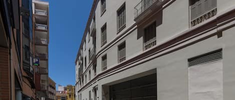 A narrow street with buildings on both sides, featuring balconies and a garage door.