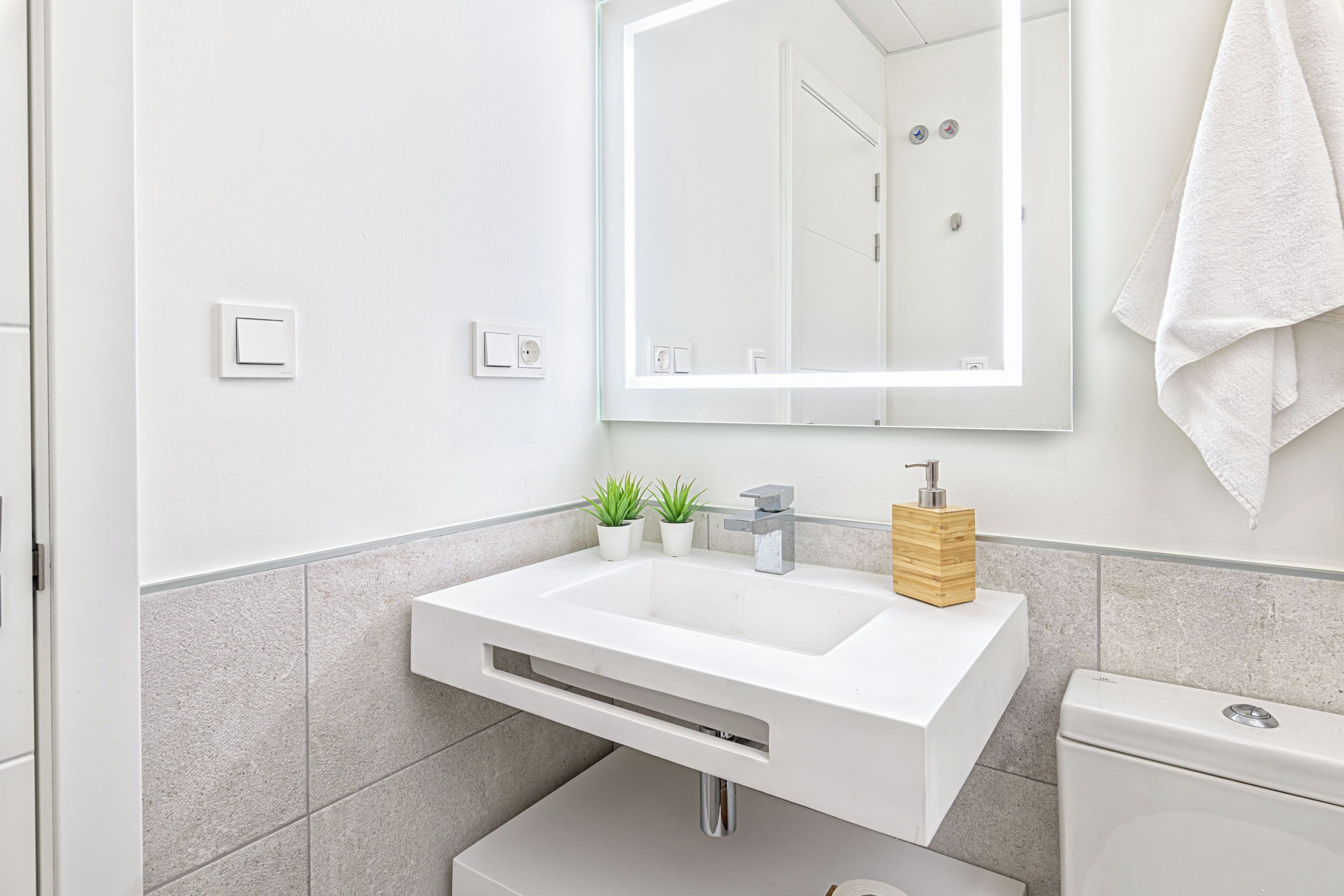 A modern bathroom with a white sink, a mirror, and a toilet.