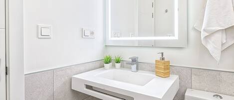 Un baño moderno con un lavamanos blanco, un espejo y un inodoro.