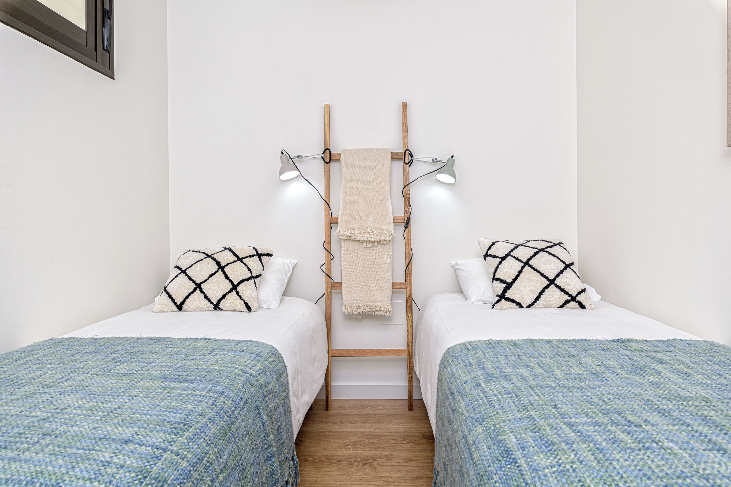 Una habitación con dos camas individuales, cada una con una colcha de diseño azul y blanco, una toalla beige colgada entre las camas y dos lámparas de pared.