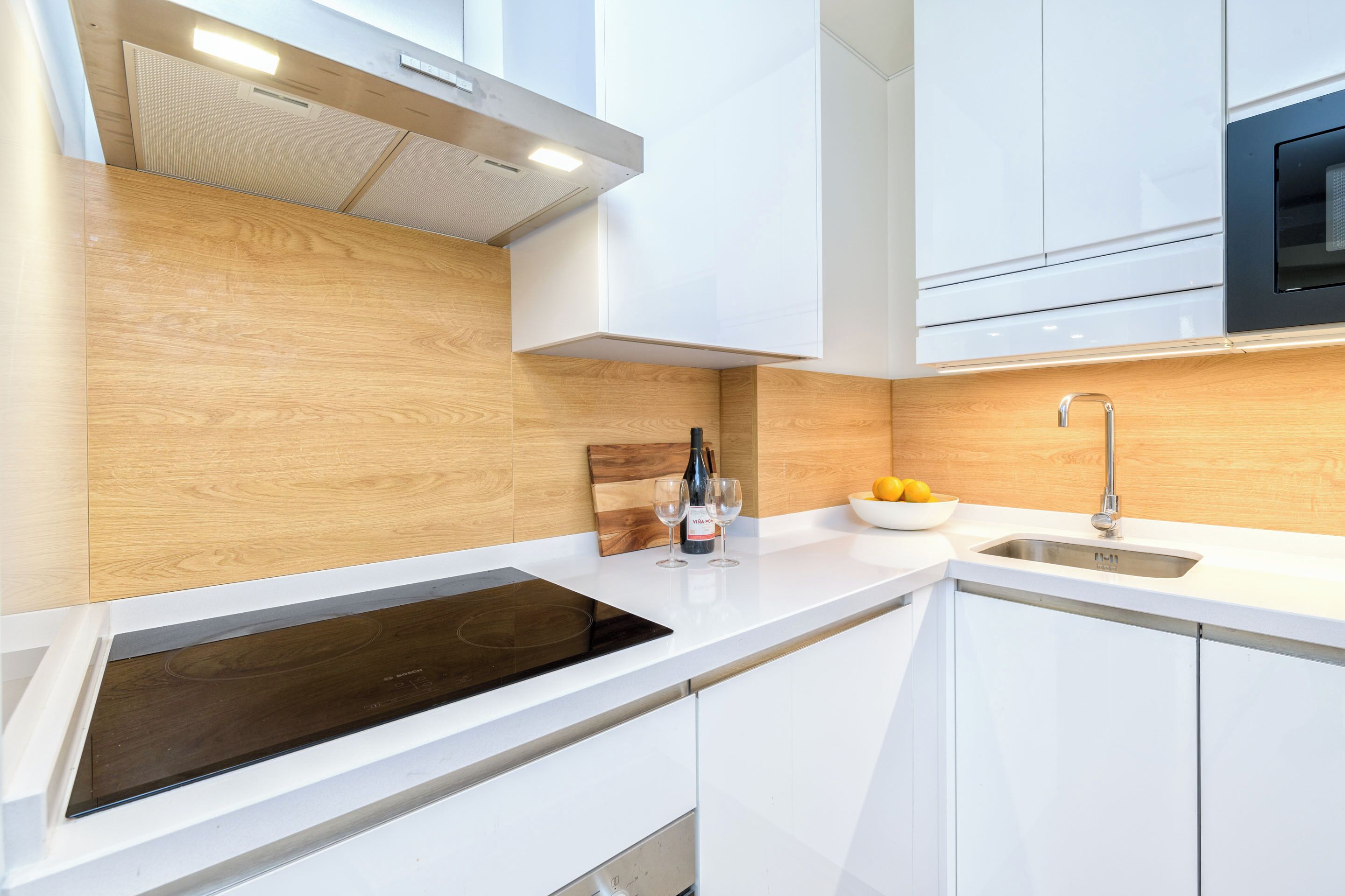 A modern kitchen with white cabinets, a wooden backsplash, a built-in oven, and a sink.