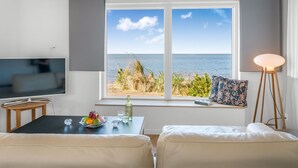 Ett rum med ett stort fönster, en tv, ett bord med frukt och glas, och en lampa.