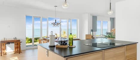 A modern kitchen with a large island, pendant lights, and a view of the ocean.