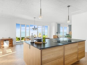 Cocina moderna con una isla grande, luces colgantes y vistas al océano.
