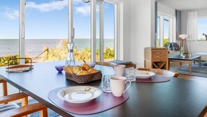 En matplats med utsikt över havet, en modern kristallkrona och ett bord dukat med tallrikar, glas och en korg med bröd.