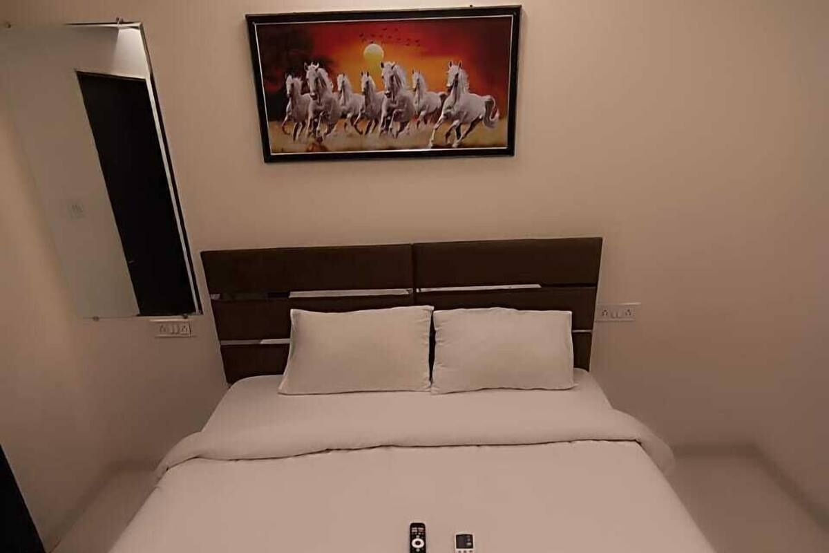 Een hotelkamer met een groot bed, een schilderij van paarden aan de muur en twee afstandsbedieningen op het bed.