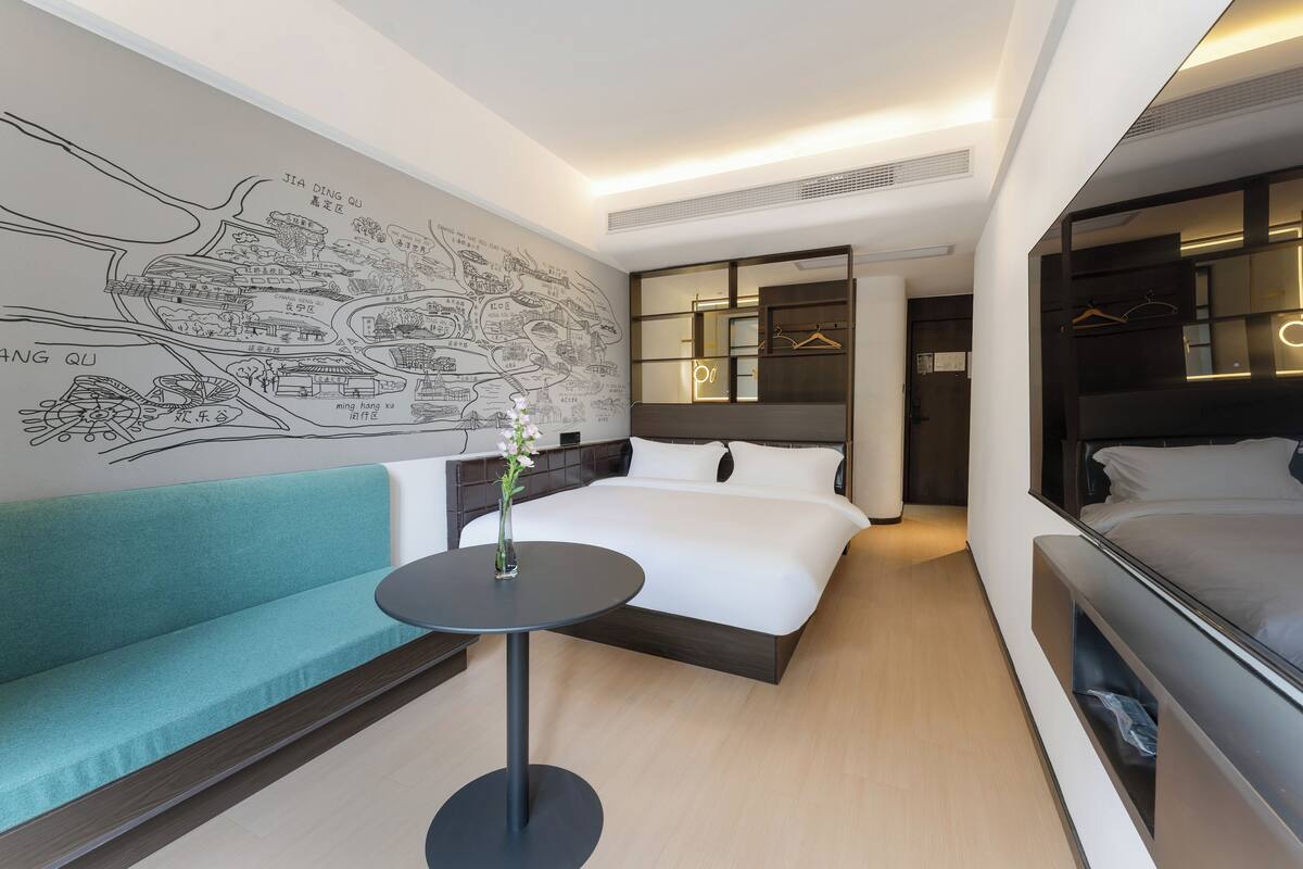Ein modernes Hotelzimmer mit einem großen Bett, einer Sitzecke, einem kleinen Tisch mit einer Vase und einem Wandbild.