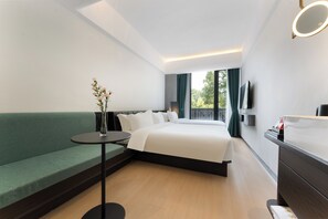 A modern hotel room with a large bed, a green sofa, a small round table with a vase, a dresser, and a TV mounted on the wall. - shanghaipudongxiangyuangguojiudian (Shanghai)
