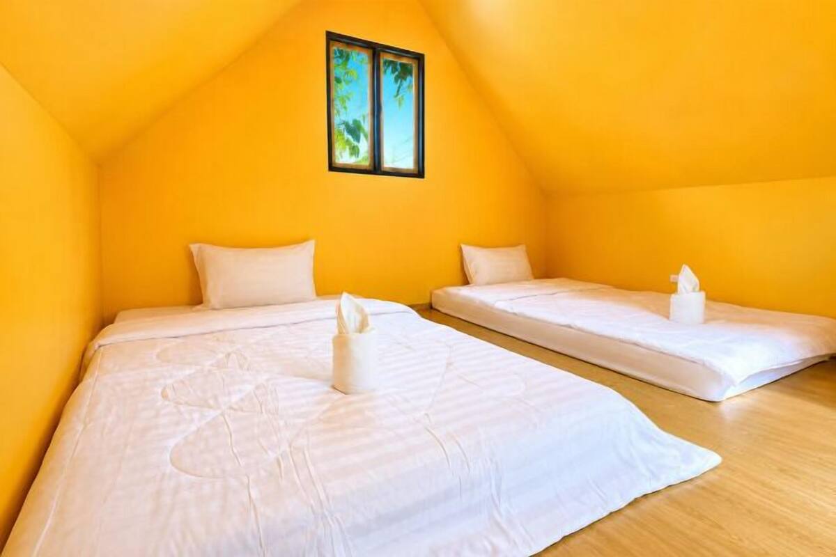 A room with two beds, a wooden floor, and a window with a view of greenery.
