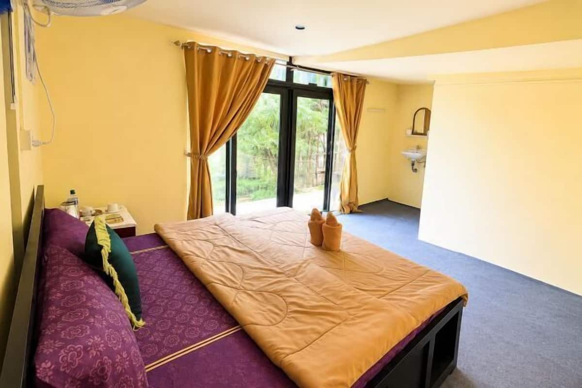Ein Zimmer mit Bett, Fenster mit Vorhängen, Waschbecken und Tür.