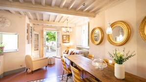 Un coin repas avec une table en bois, des chaises et un vase de fleurs. On y trouve également un canapé et une fenêtre donnant sur un paysage verdoyant.
