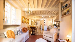 Un vaste espace de vie comprenant un canapé, un fauteuil et un pouf, une table à manger avec des chaises, et une cuisine en arrière-plan.