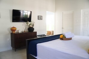 A hotel room with a bed, a television on the wall, a dresser, and a door. - Spacious Private Villa Near Ocho Rios, Jamaica | Sleeps 6 ⭐ (St. Mary Parish)