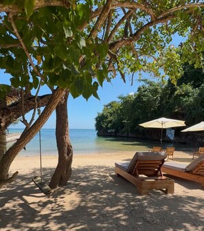 A beach with wooden lounge chairs and umbrellas, a swing, and a view of the ocean. - Spacious Private Villa Near Ocho Rios, Jamaica | Sleeps 6 ⭐ (St. Mary Parish)