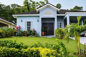 A light blue house with a dark front door, a small porch, and a well-maintained garden.