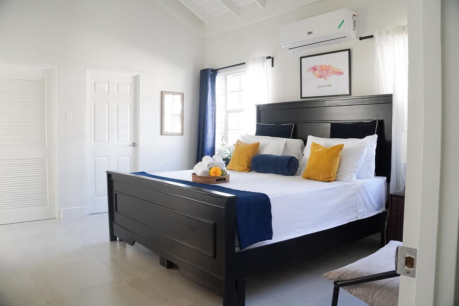 A bedroom with a bed, a bedside table, a wall-mounted air conditioner, and a framed map.