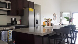 A modern kitchen with dark cabinets, a stainless steel refrigerator, a stove, and a coffee maker.