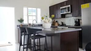 A modern kitchen with dark cabinets, a stainless steel microwave, a large island with bar stools, and a vase with flowers.