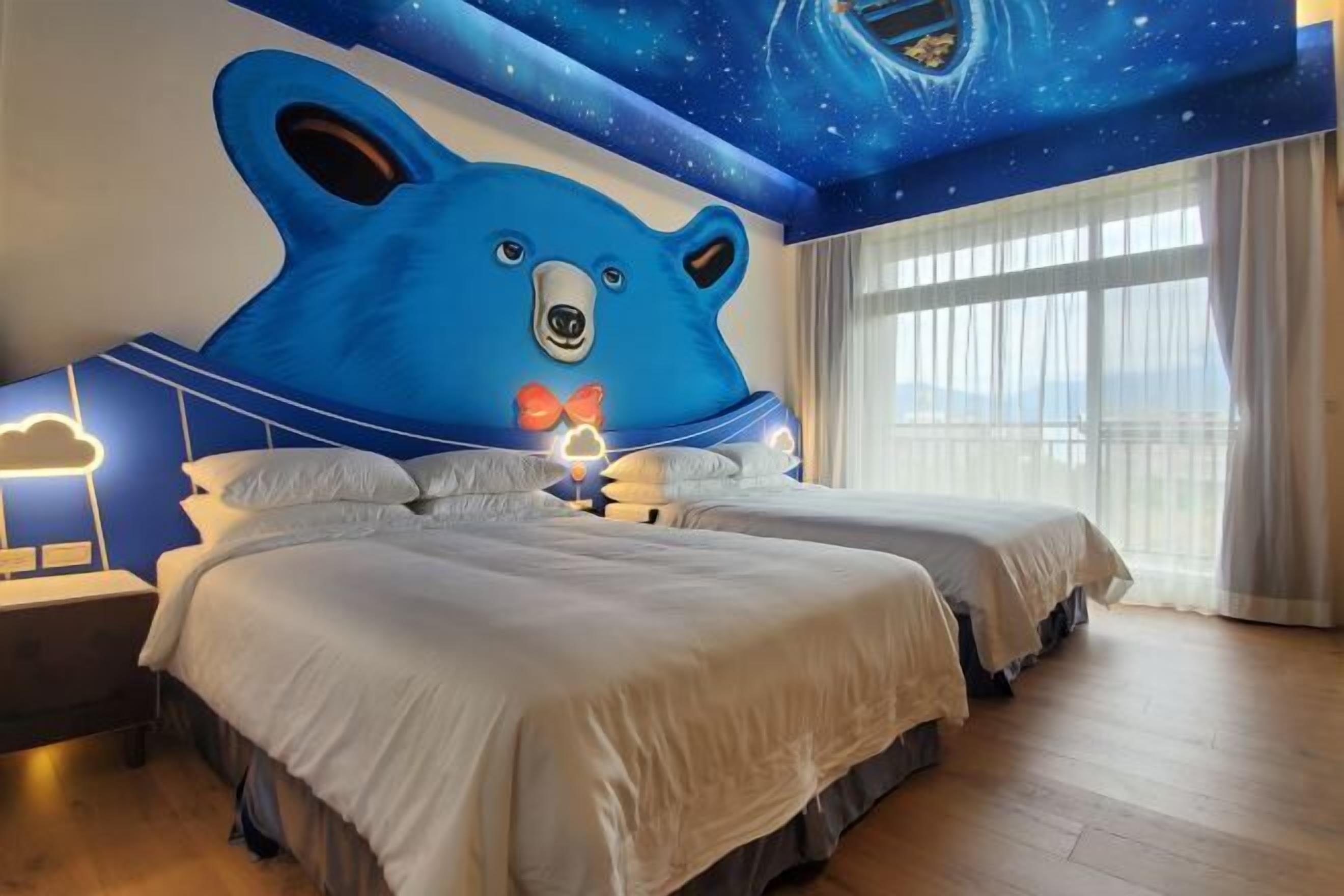 A hotel room with two beds, a large bear mural on the ceiling, and a night sky design.