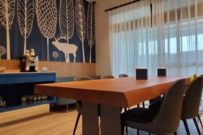 Un comedor con una mesa y sillas de madera, una máquina de café y una pared decorativa con motivos de hojas.