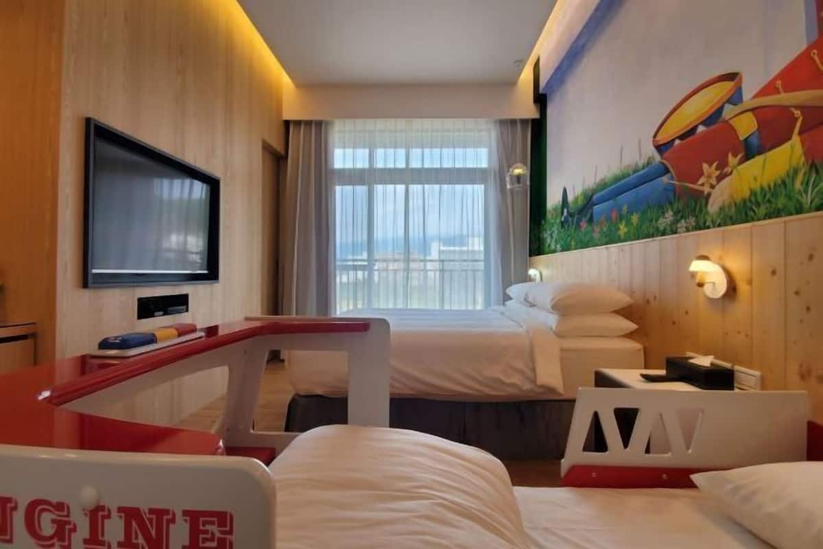 A hotel room with a bed, a TV, a painting, and a window with curtains.