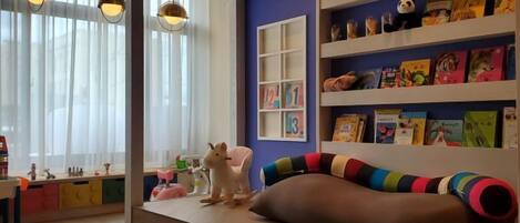 A children's play area with a sofa, shelves with books, and a cat statue.