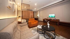A modern living room with a sofa, armchair, coffee table, TV, and a desk with a chair. - Jiangmen Mintai Hotel (Jiangmen)